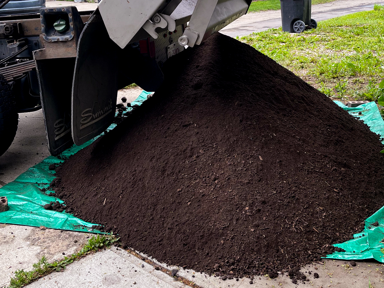 Freshly dumped pile of soil on driveway, ready to be spread and used for planter filling.